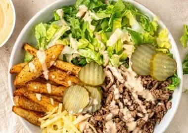 A colorful bowl featuring fresh ingredients of a burger bowl, including lettuce, tomatoes, and beef.