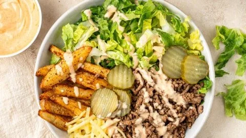 A colorful bowl featuring fresh ingredients of a burger bowl, including lettuce, tomatoes, and beef.