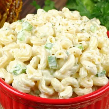 Creamy deli-style macaroni salad served in a bowl, garnished with herbs.