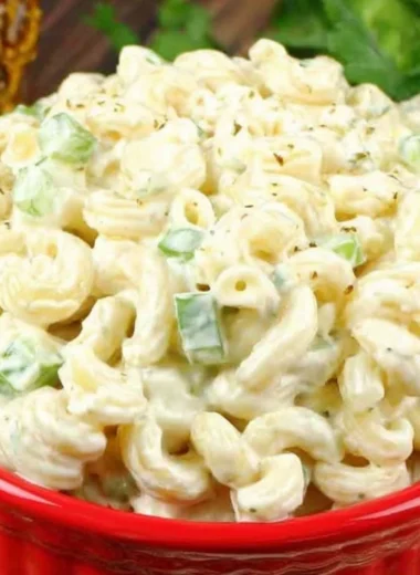 Creamy deli-style macaroni salad served in a bowl, garnished with herbs.