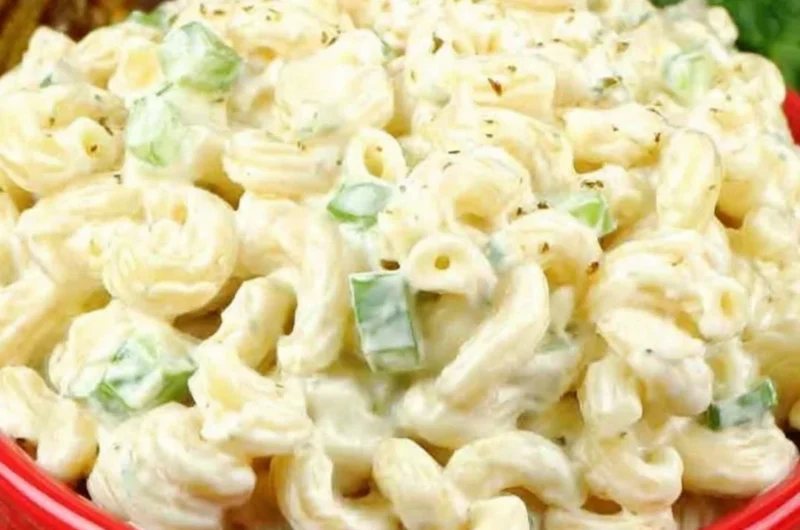 Creamy deli-style macaroni salad served in a bowl, garnished with herbs.
