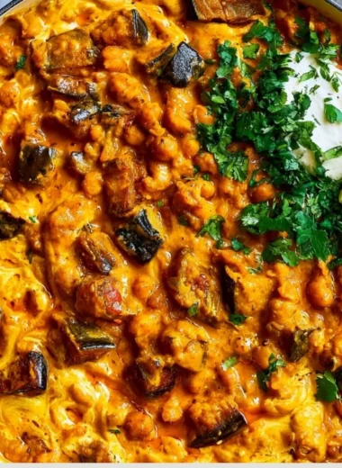 Bowl of easy eggplant curry on a wooden table with fresh herbs and spices.