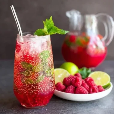Raspberry Mojito cocktail garnished with mint and lime on a wooden table