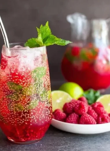 Raspberry Mojito cocktail garnished with mint and lime on a wooden table